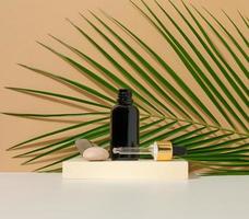 brown glass bottle with a pipette stands on a brown background. Container for cosmetics, serum and oil. Palm leaf photo