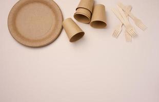 Brown paper cups and plates on a beige background. Recyclable garbage, rejection of plastic, top view photo