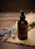 A glass brown bottle with a pipette and a bouquet of lavender on a brown wooden table. photo