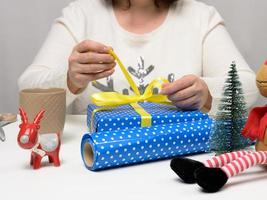 woman in a white sweater sits at the table and wraps gifts for Christmas. Preparing for the holidays photo