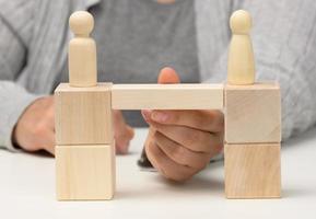 wooden figures stand on the bridge from the sides opposite each other, concept of finding a compromise, constructive dialogue, business opponents photo