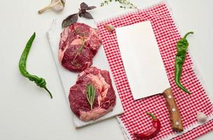raw piece of beef ribeye with rosemary, thyme on a white table photo