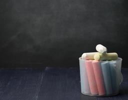 plastic bucket with colorful chalk on empty black chalk board background, back to school photo