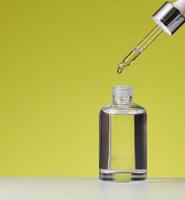 essential oil falling from the amber glass dropper. White bottle of cosmetic oil with a pipette, green background photo