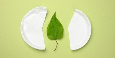 broken white plastic plate and green leaf on a green background. The concept of avoiding plastic photo