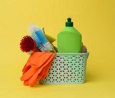 blue plastic basket with brushes, sponges and rubber gloves for cleaning, yellow background