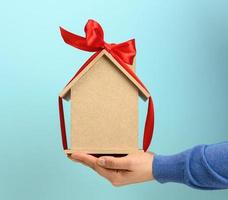 female hands hold a model of a wooden house tied with a red silk ribbon on a blue background photo