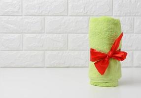 rolled up terry green towel tied with red silk ribbon on white shelf in bathroom photo