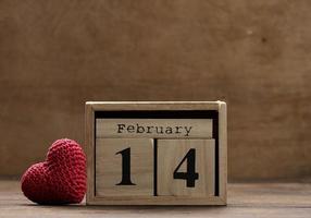 wooden calendar with date February 14 and red knitted heart, brown background photo