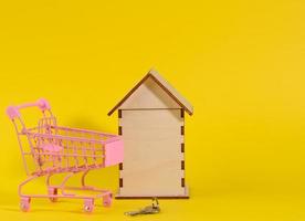 wooden house and metal miniature cart on a yellow background. Real estate purchase concept photo