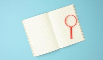 paper notebook with blank white sheets and a red magnifier on a blue background. Background for inscriptions photo