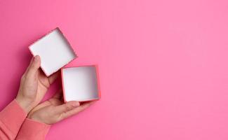 female hands holding open square cardboard gift box on pink background, top view photo