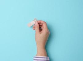 mano femenina y yeso adhesivo médico marrón para el tratamiento de lesiones y cortes en la piel, fondo azul foto