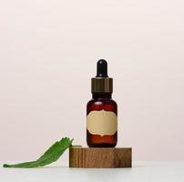 A brown glass bottle with a paper label and a pipette on a white table. Containers for cosmetics photo