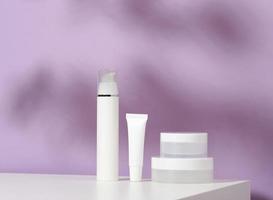 jar and empty white plastic tubes for cosmetics on a purple background. Packaging for cream, gel, serum, advertising and product promotion, mock up photo