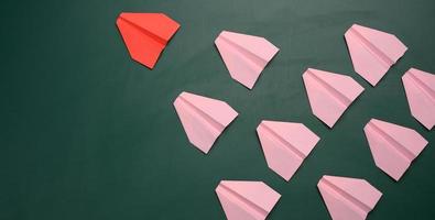 a group of pink paper airplanes follow the first red airplane against a green background photo