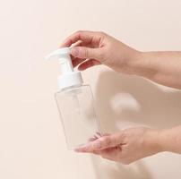female hand holds empty plastic container with dispenser for liquid products, soap or shampoo on beige background photo
