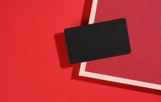 la tarjeta de visita rectangular negra en blanco se encuentra sobre un fondo rojo moderno con hojas rojas de papel con una sombra. plantilla de negocio foto