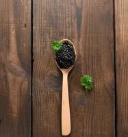 fresh grainy black paddlefish caviar in brown wooden spoon on a black background, top view photo