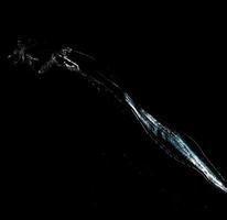 jet of transparent water with small drops and splashes on a black background photo