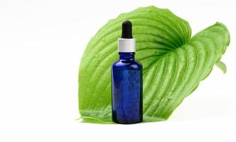 blue glass transparent bottle with a pipette on the background of a green leaf. Natural cosmetics concept photo