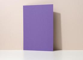 hoja de papel de cartón púrpura en blanco con sombra en la mesa blanca. plantilla para volante, anuncio