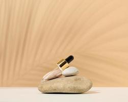 a glass pipette for a cosmetic bottle lies on a stack of stones, the shadow of a palm leaf photo