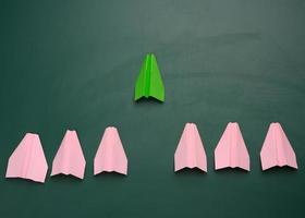 group of pink paper planes follow the first green airplane against a green background. The concept of uniting a team to achieve goals photo