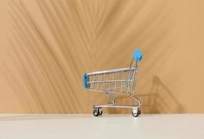 empty miniature shopping cart on brown background. Seasonal sale, copy space, online shopping photo