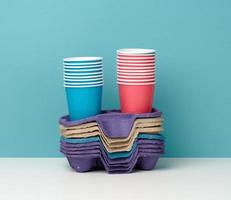 stack of paper disposable multi-colored cups and stand on white table, blue background photo