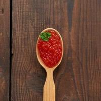 red caviar of pink salmon lies in a wooden spoon. Brown wooden table, top view photo