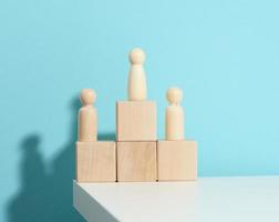 wooden figures of men stand on a pedestal of their cubes on a blue background. The concept of rivalry in sports, business and life. Achieving success and leadership photo