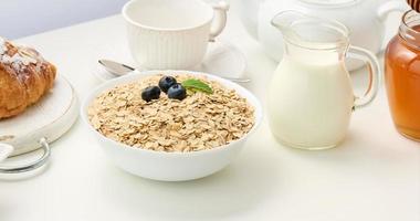 Raw oatmeal in white ceramic plate on white table, breakfast, close up photo