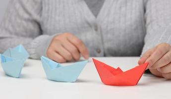 un grupo de barcos de papel azul sigue a un barco rojo frente a un fondo blanco. el concepto de un líder fuerte y carismático en un equipo, manipulando a las masas foto