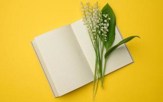 cuaderno abierto con sábanas blancas en blanco y un ramo de lirios florecientes del valle sobre un fondo amarillo foto