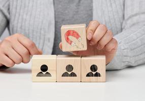 female hand holds a wooden cube with a magnet over the cubes with little men, recruiting for a strong team. Open vacancies in the company photo