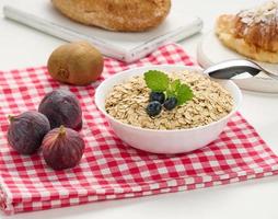 avena cruda en plato de cerámica blanca y frutas en mesa blanca, desayuno foto