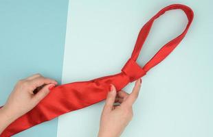 two female hands hold a red silk tie on a blue background photo