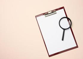 folder with blank white sheets and a black magnifier on a beige background. Background for inscriptions photo