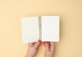 two female hands hold an open notebook with blank white sheets on a beige background photo