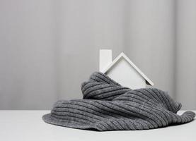 white wooden miniature house wrapped in a gray knitted scarf. Building insulation concept, loans for repairs photo