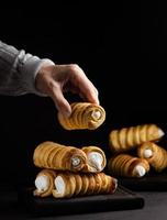 A woman's hand holds a baked tube with whipped protein cream, black background photo