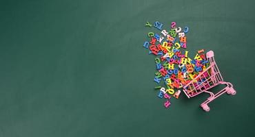 scattered multicolored letters of the english alphabet from a miniature shopping cart on a green background photo