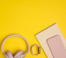 pink wireless headphones, smartphone and smart watch on a yellow background photo