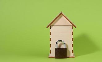 miniature wooden house and metal lock on a green background, security concept photo