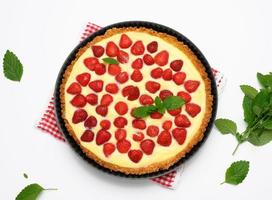 baked round tart with strawberries and tender milk cream on a white table background photo