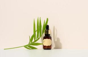 brown glass bottle with a pipette stands on a brown background. Container for cosmetics, serum and oil, palm leaf photo