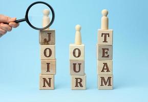 wooden figurines of men stand on cubes with the inscription and a hand with a magnifying glass on a blue background photo