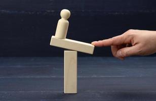 a wooden figure of a man stands on a swing, his finger keeps balance. Concept of help photo