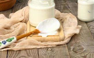 homemade yogurt in a glass transparent jar on a wooden table, a healthy fermented milk product photo